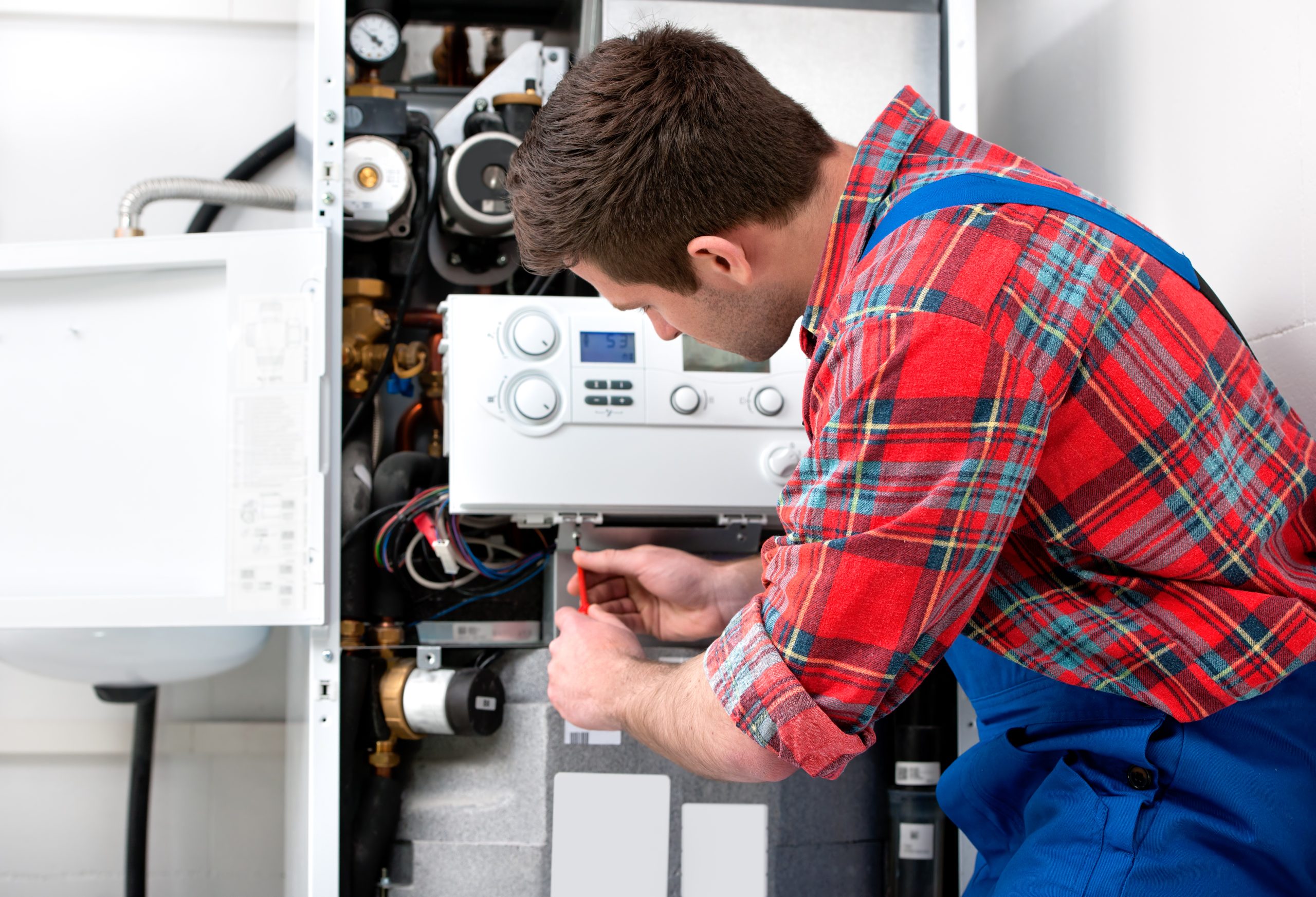 Man in overalls expertly repairs a gas furnace, highlighting his HVAC maintenance skills.