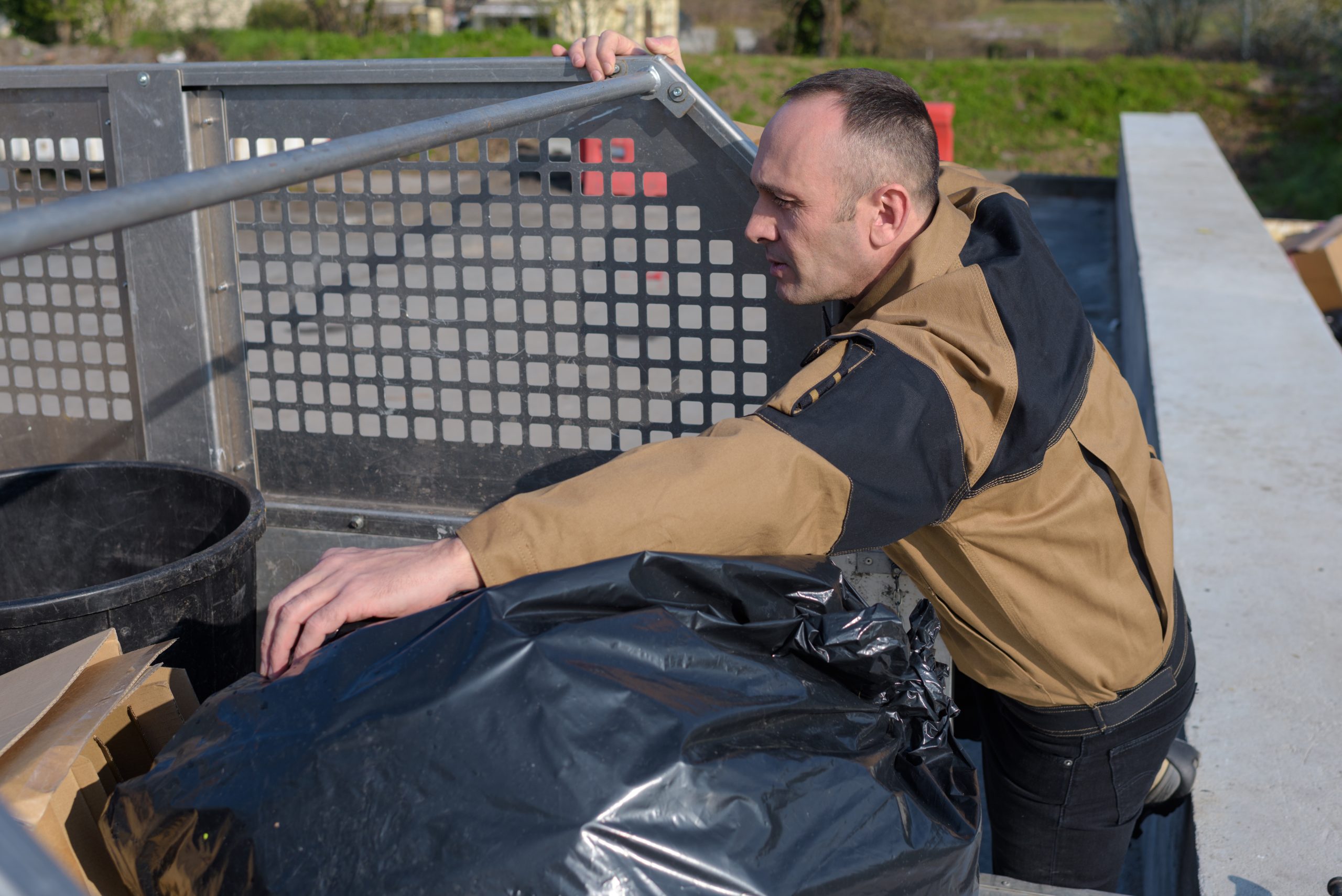 Maintenance man helping keep the city clean Man loads trash bags into a garbage truck on a sunny day, helping keep the community clean