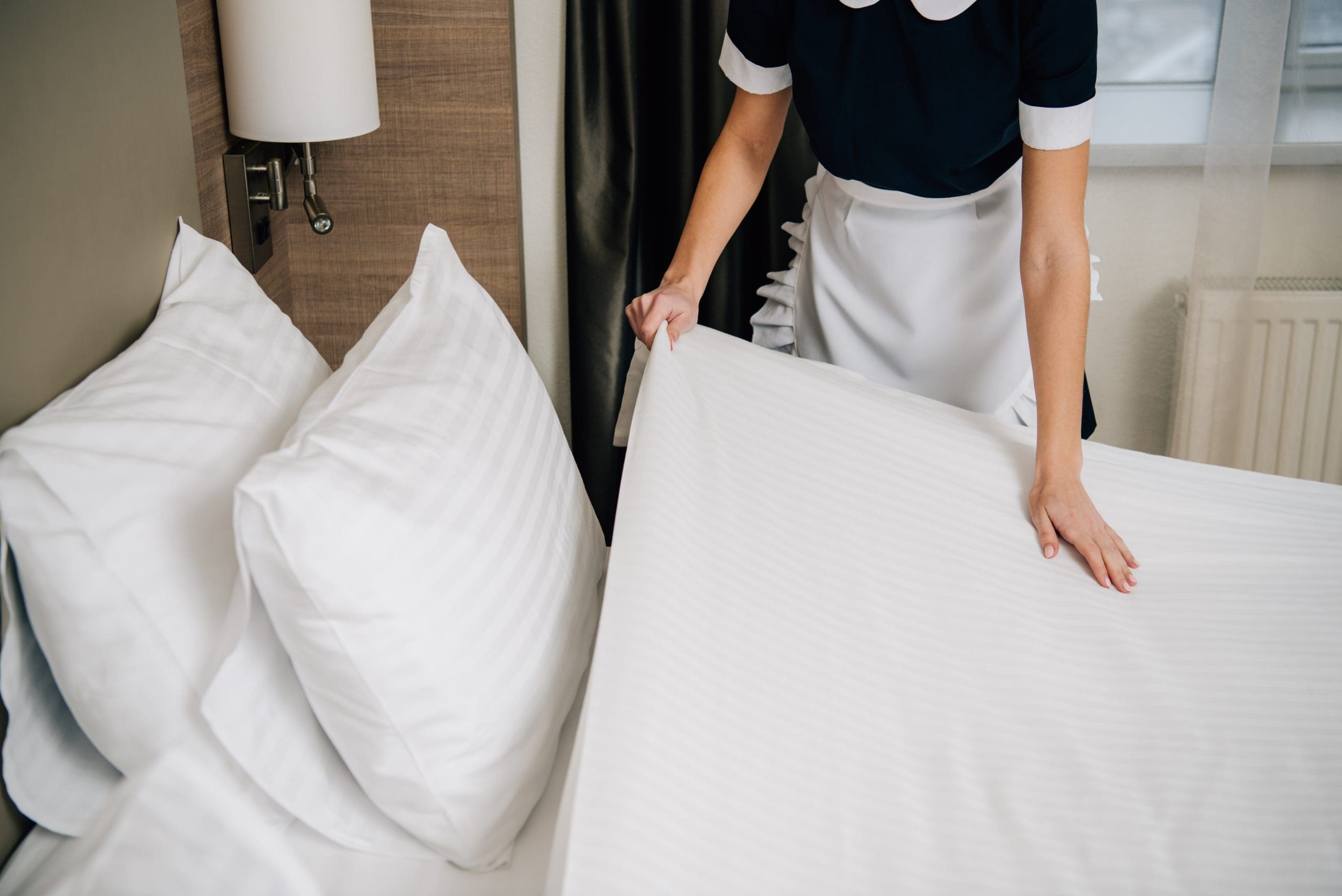 A maid places a white pillow on a neatly made bed, enhancing the room's tidy look.